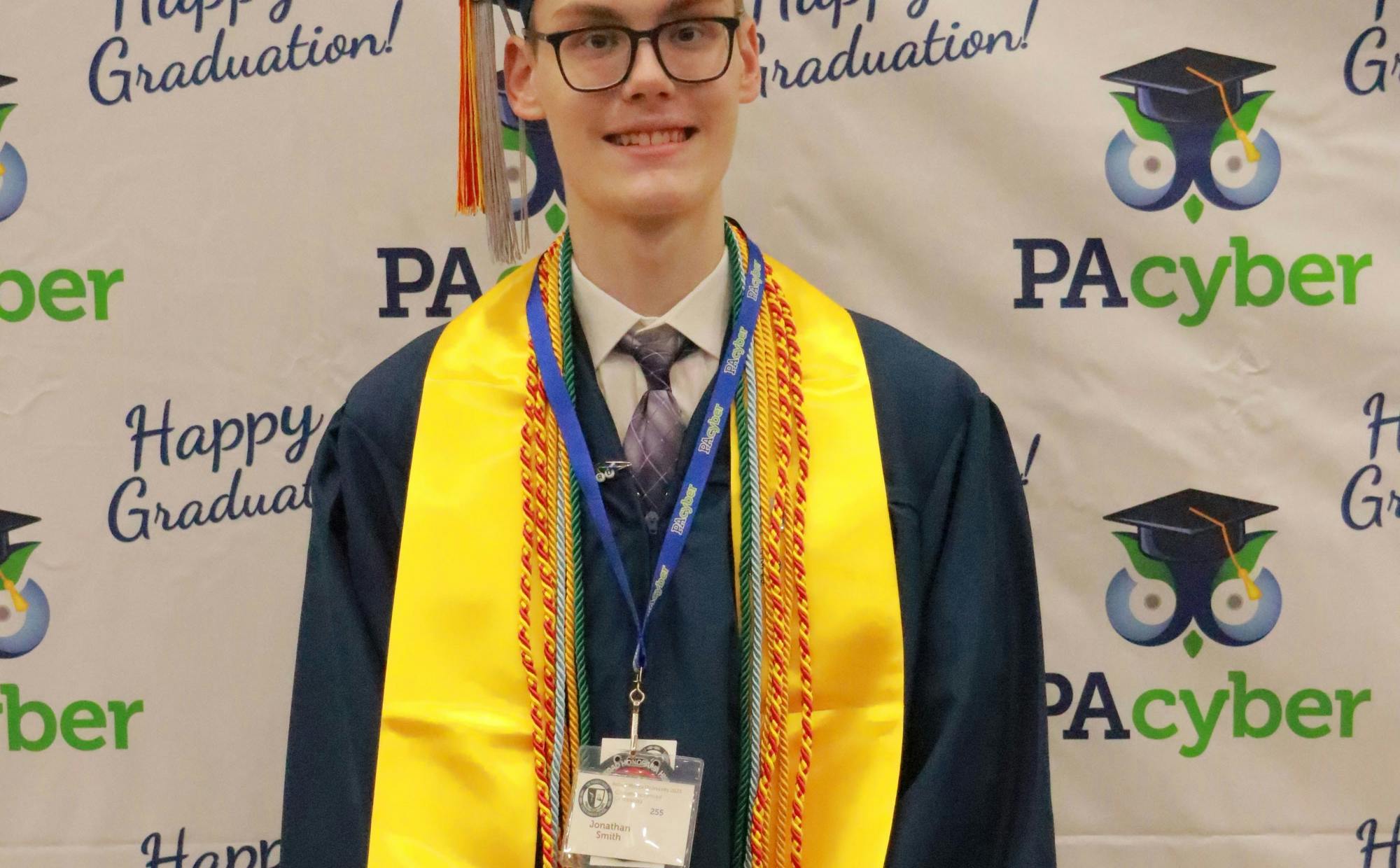 PA Cyber graduate wears cap and gown and several colorful cords.